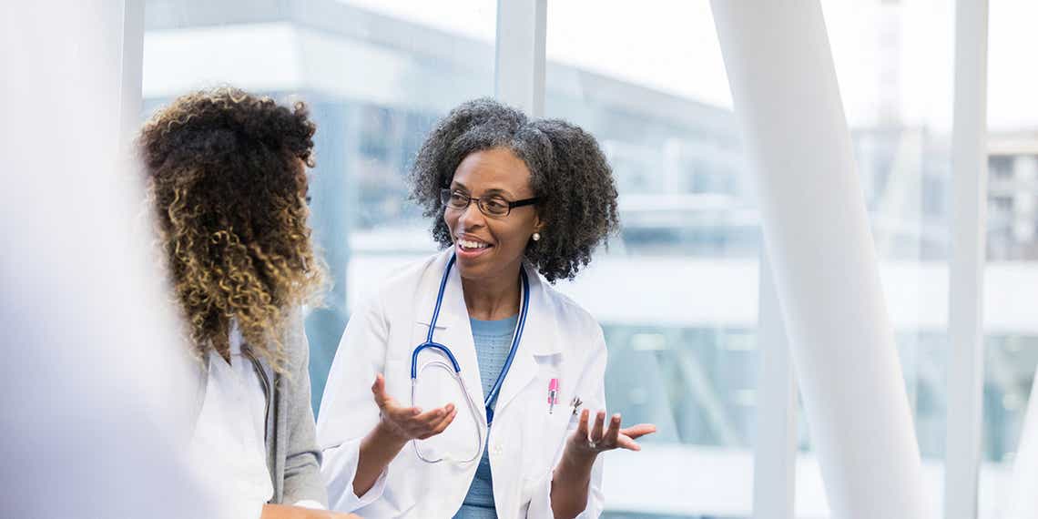 a female doctor discusses a new solution with a healthcare sales professional in the hallway of a medical facility