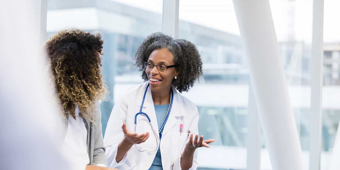 a female doctor discusses a new solution with a healthcare sales professional in the hallway of a medical facility