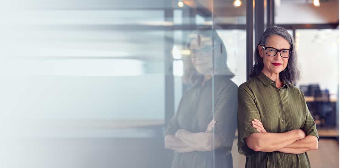 senior sales leader leaning against a glass wall looking at the camera happy with the changes she is successfully leading her sales organization through as a result of the skills she built in the leaders leading change training program