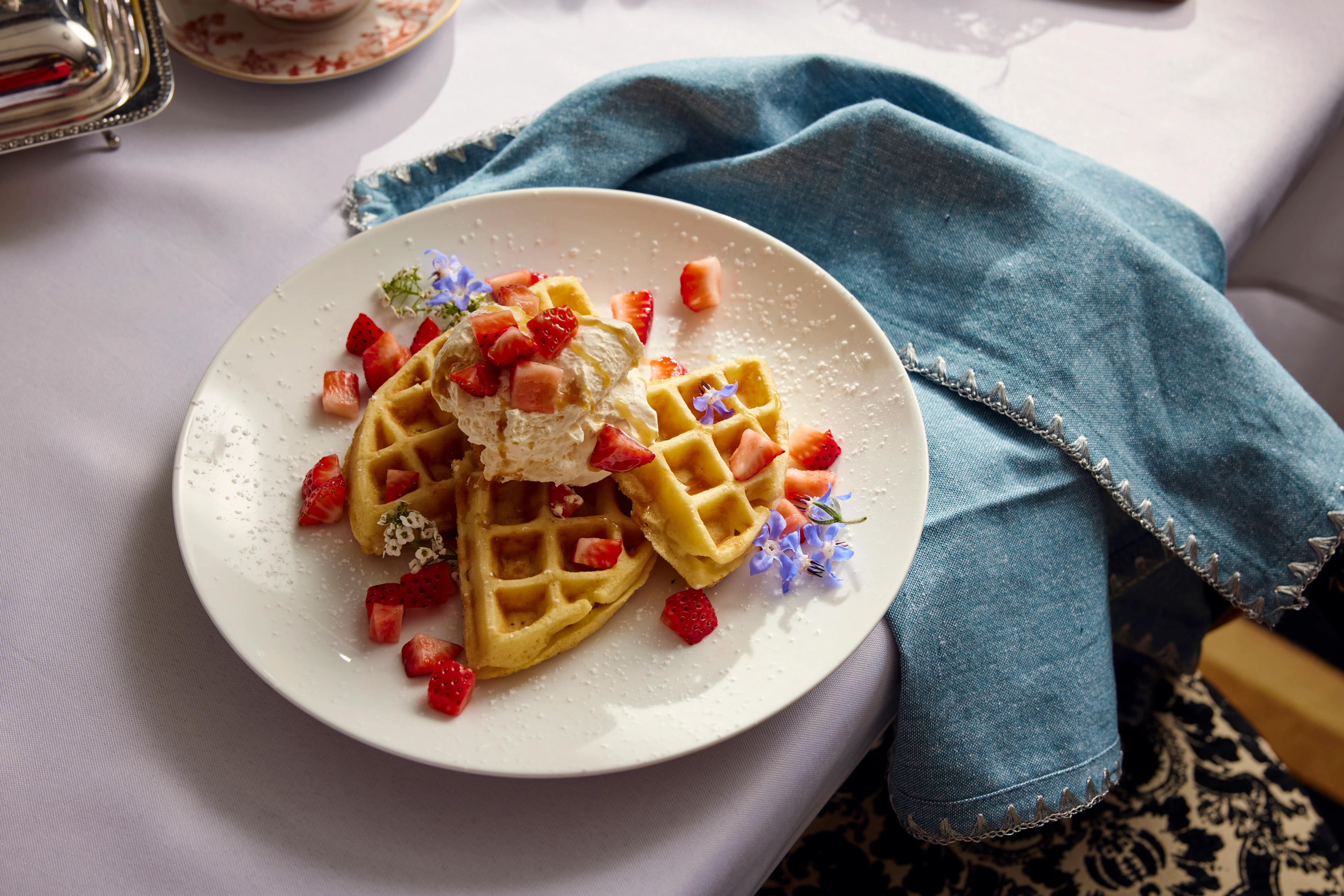 An elegant waffle on a plate with butter, fruit, and flowers.