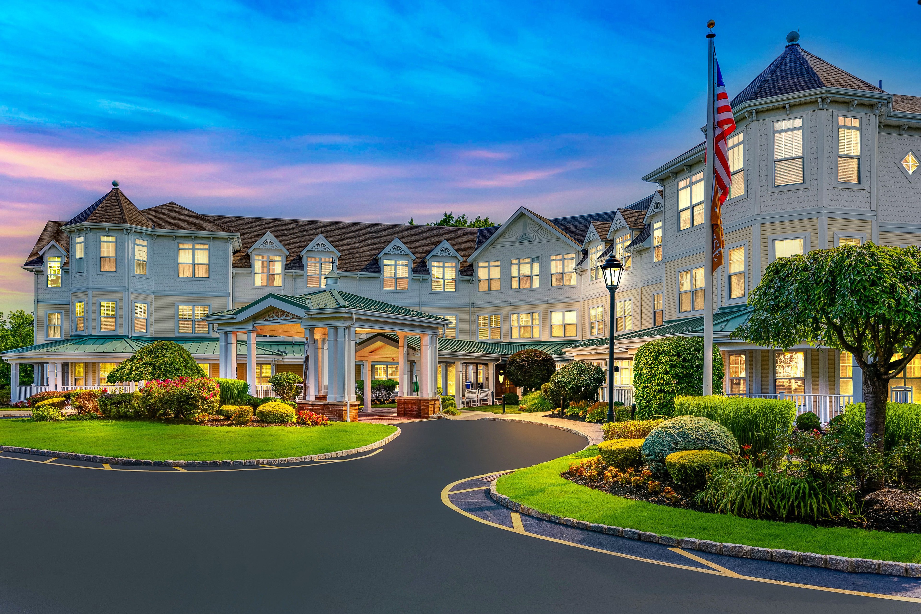 The front of a luxurious senior living facility at night with the lights on.
