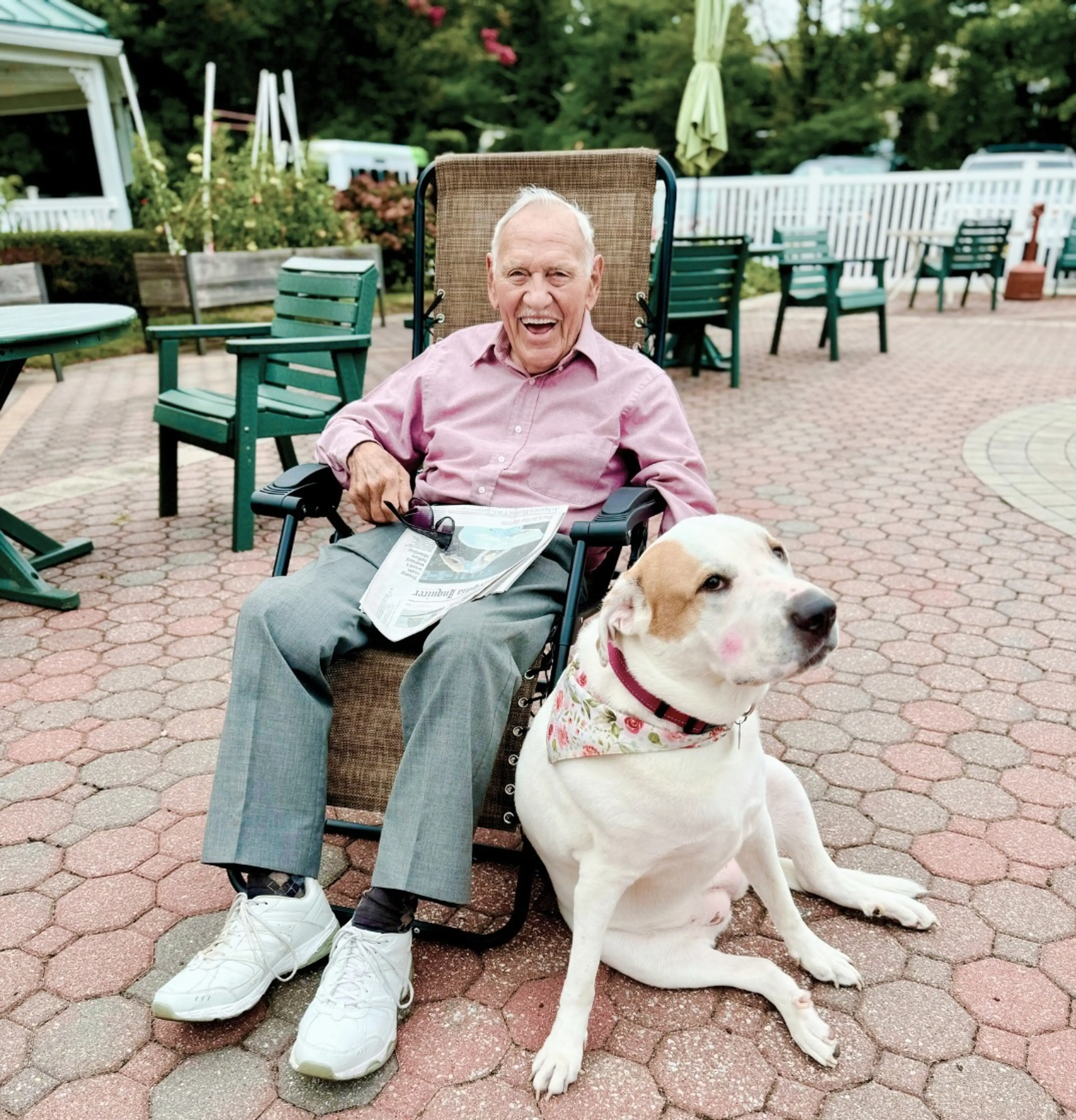 A senior sitting outside on a chair next to his dog.