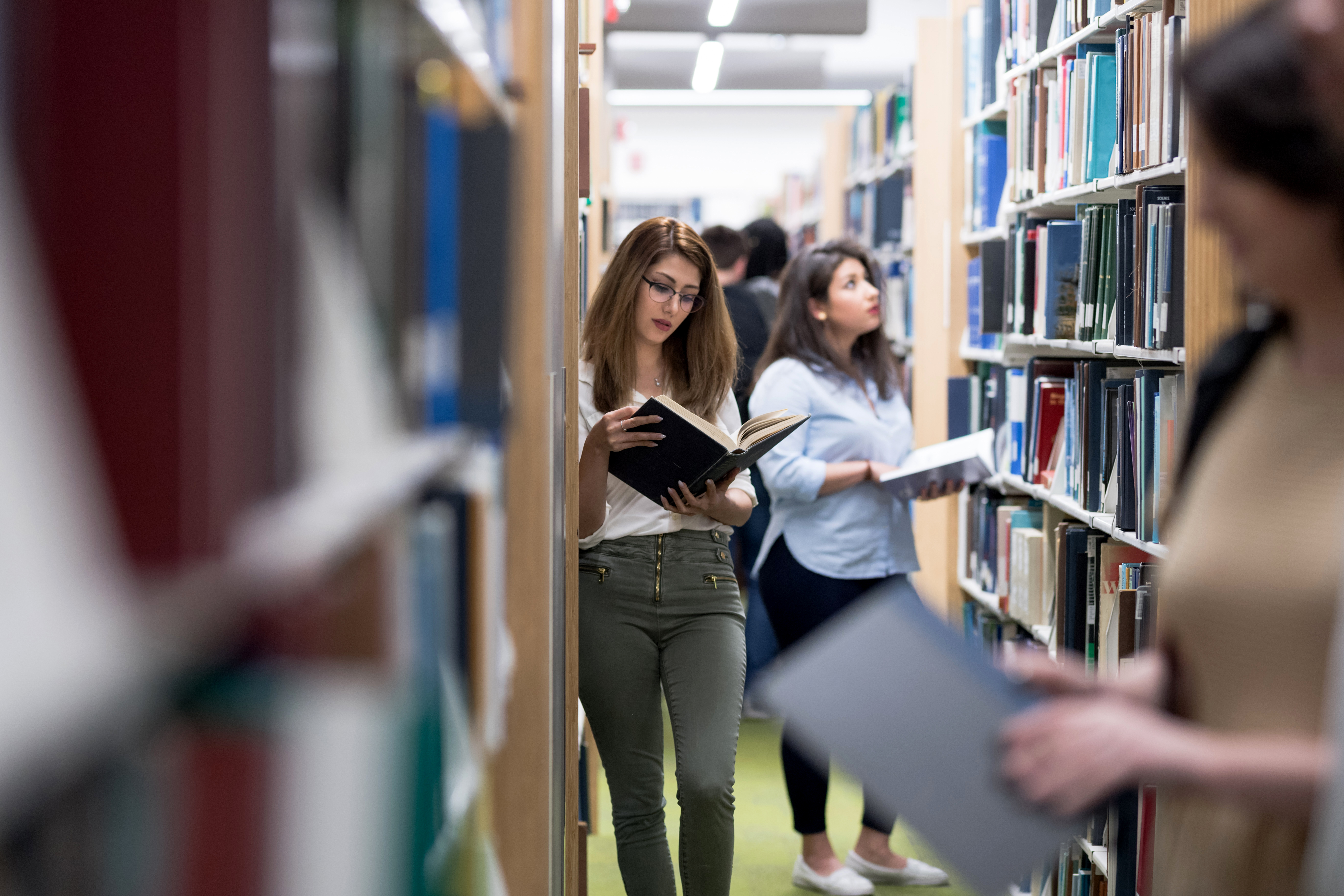 Frau liest in Bibliothek ein Buch.