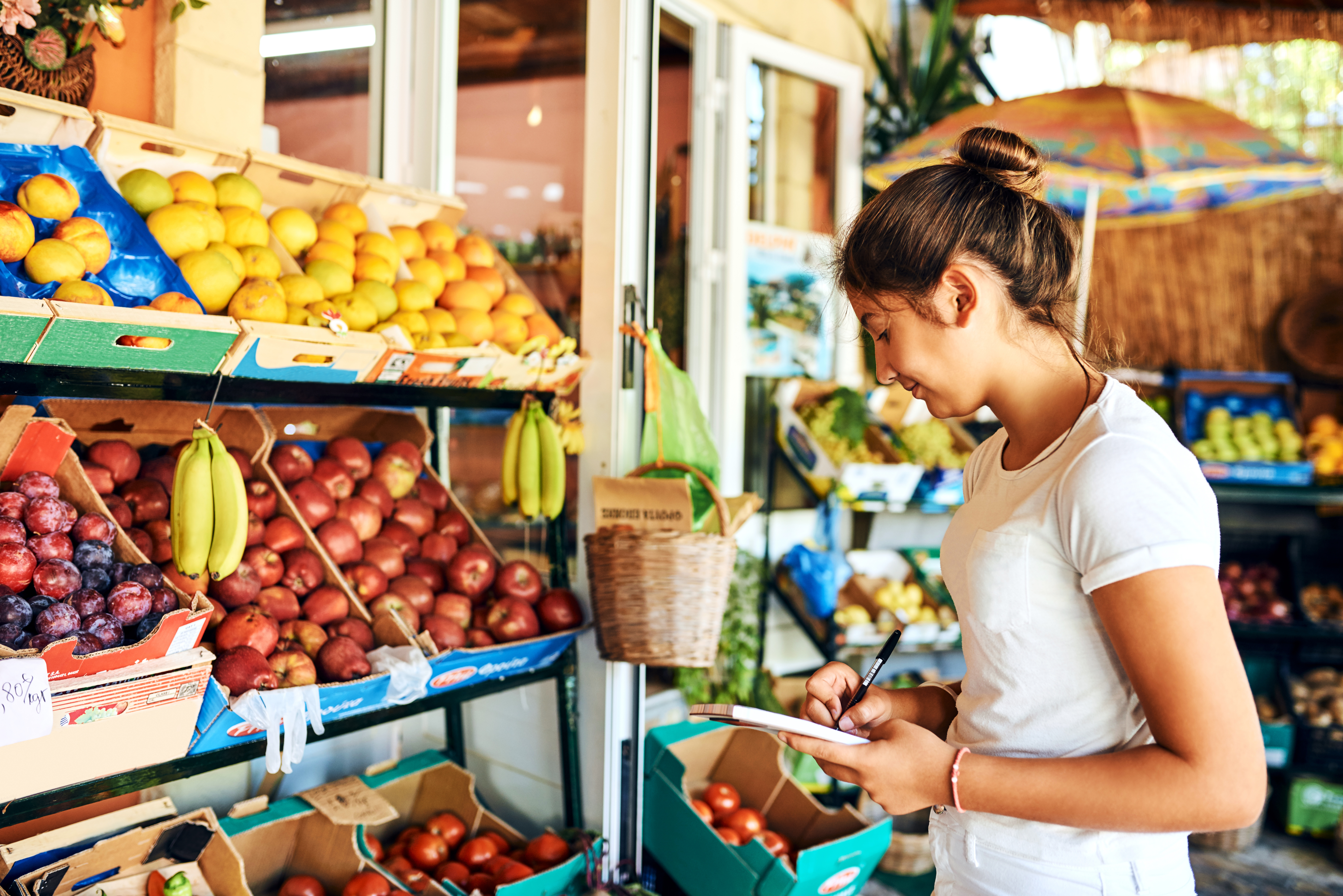 A young woman standing in front of a shelf with fruits.
