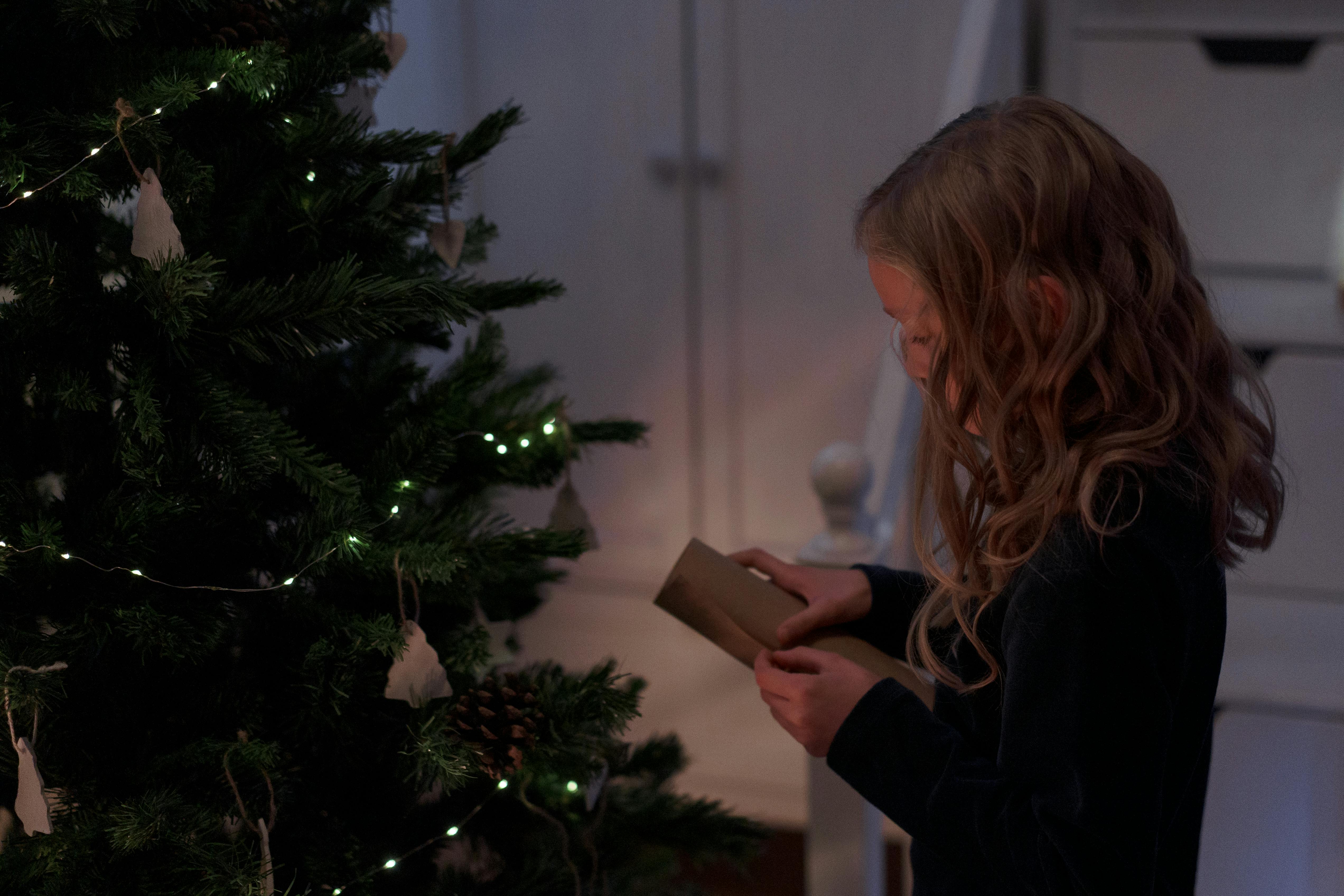 Kind rollt Brief am Tannenbaum aus.