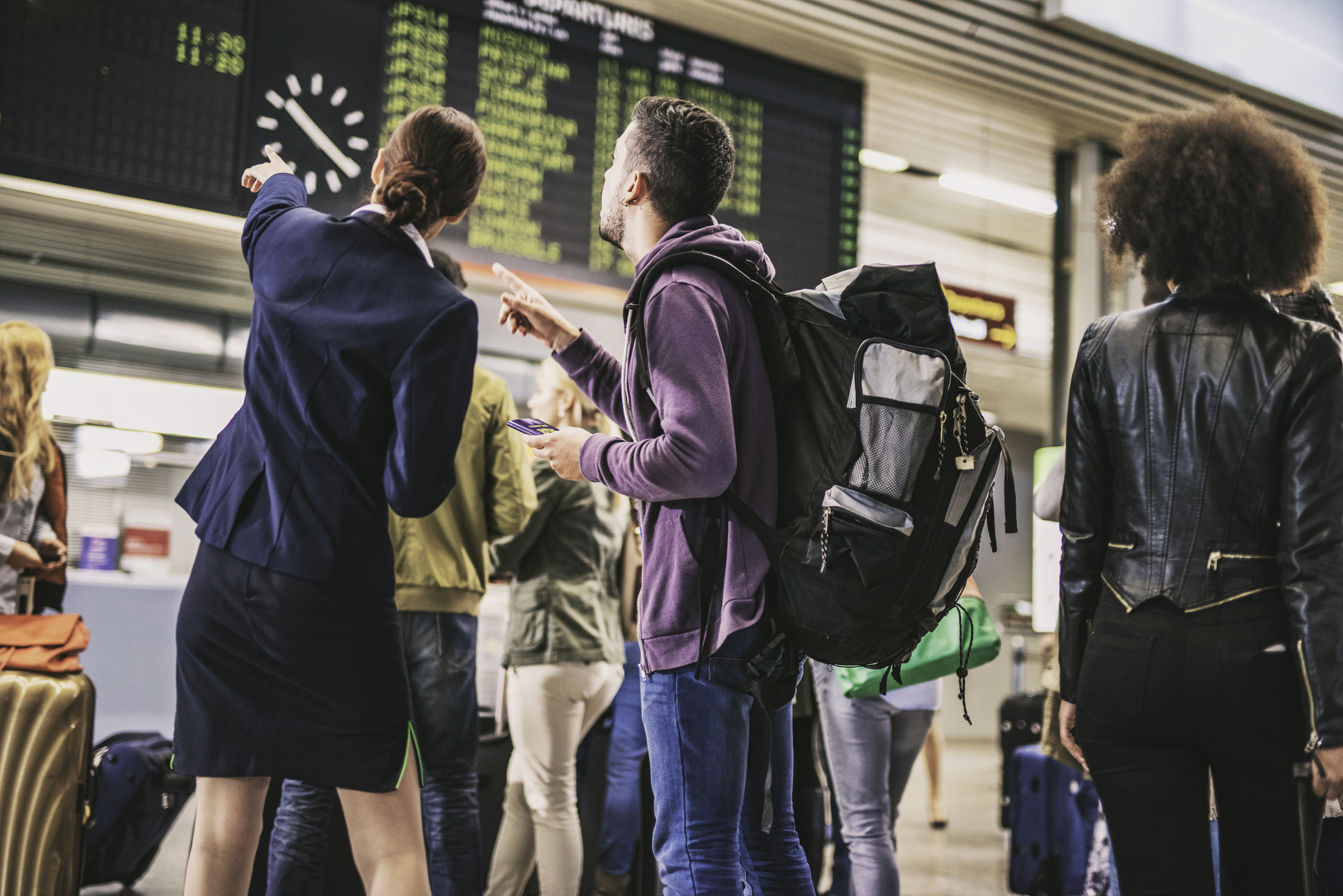 Mehrere Personen stehen am Flughafen zusammen und schauen auf die Anzeigetafel.