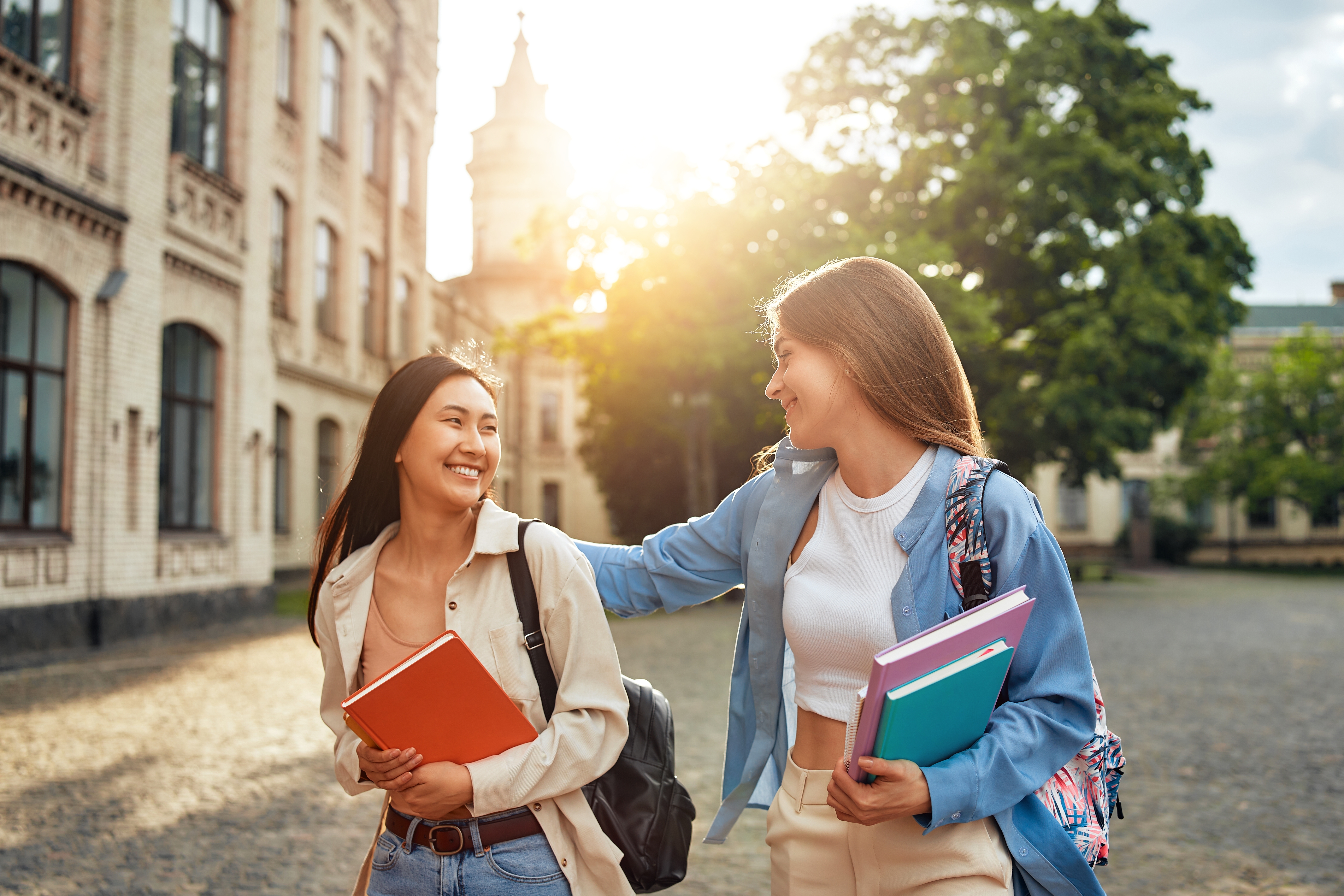 Zwei Mädchen haben Bücher in der Hand und lachen sich draußen an.