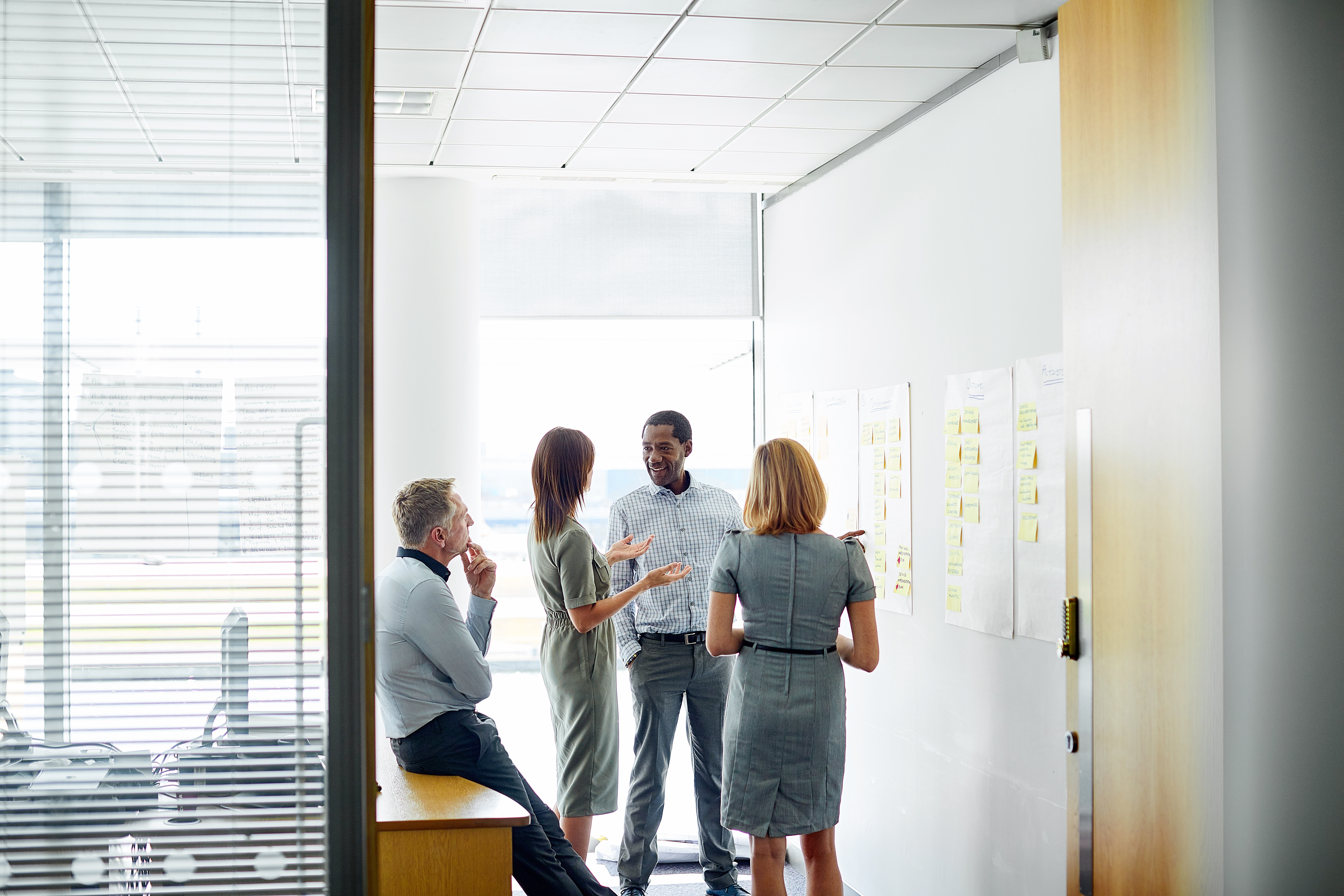Vier Personen besprechen ein Projekt an einer Wand