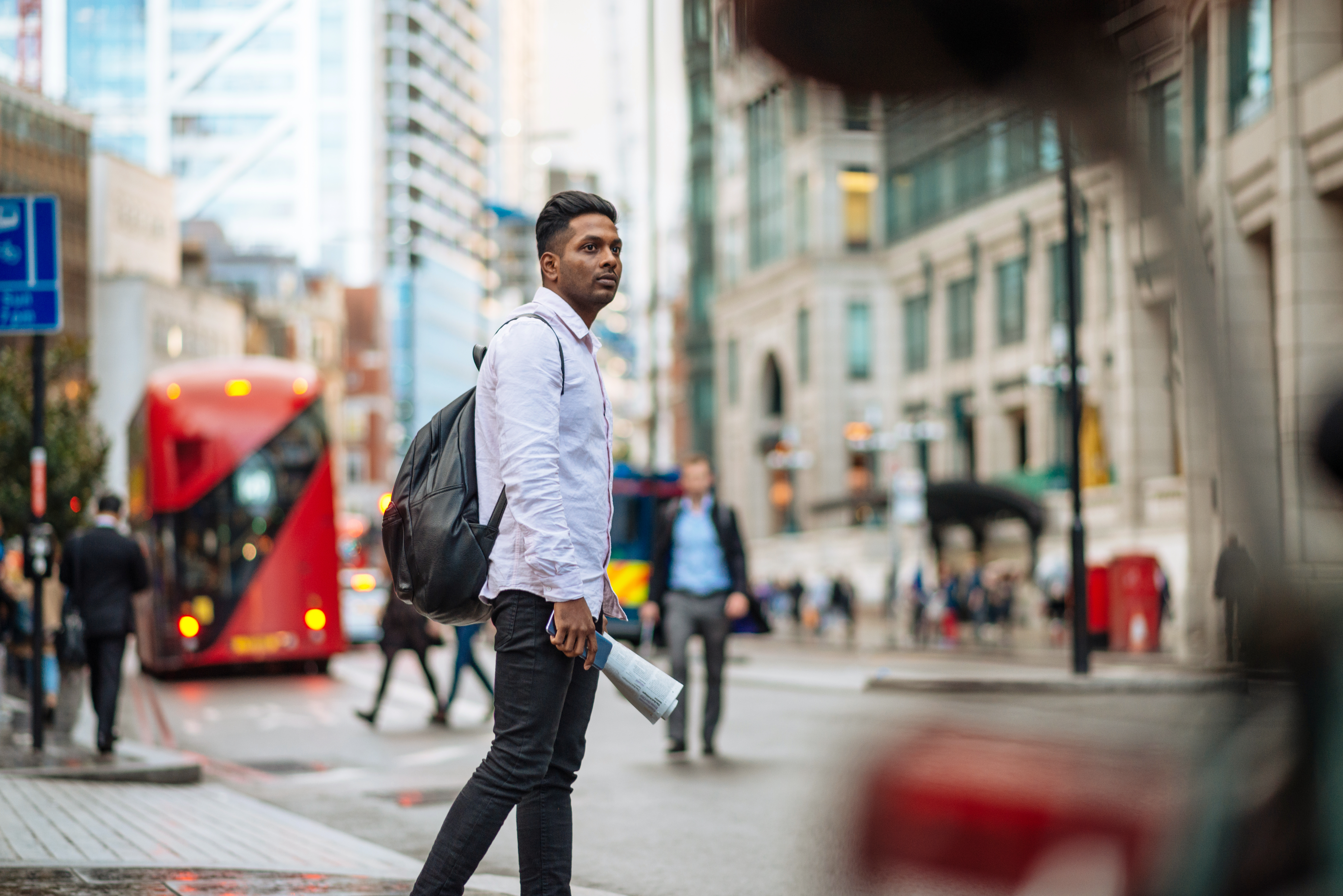 A man walking across a road in a large city.