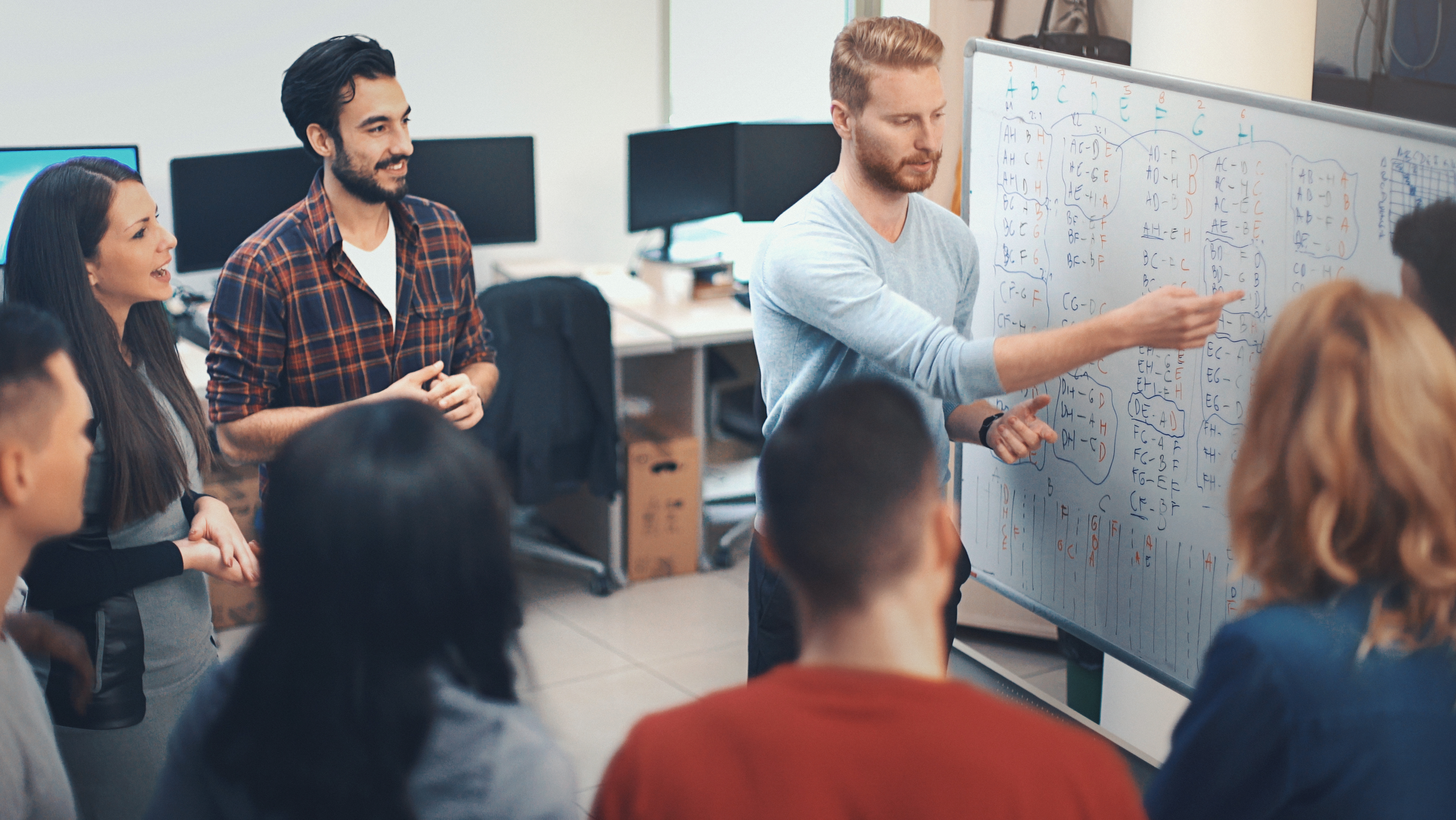Mehrere Personen stehen vor einem Whiteboard und besprechen etwas.