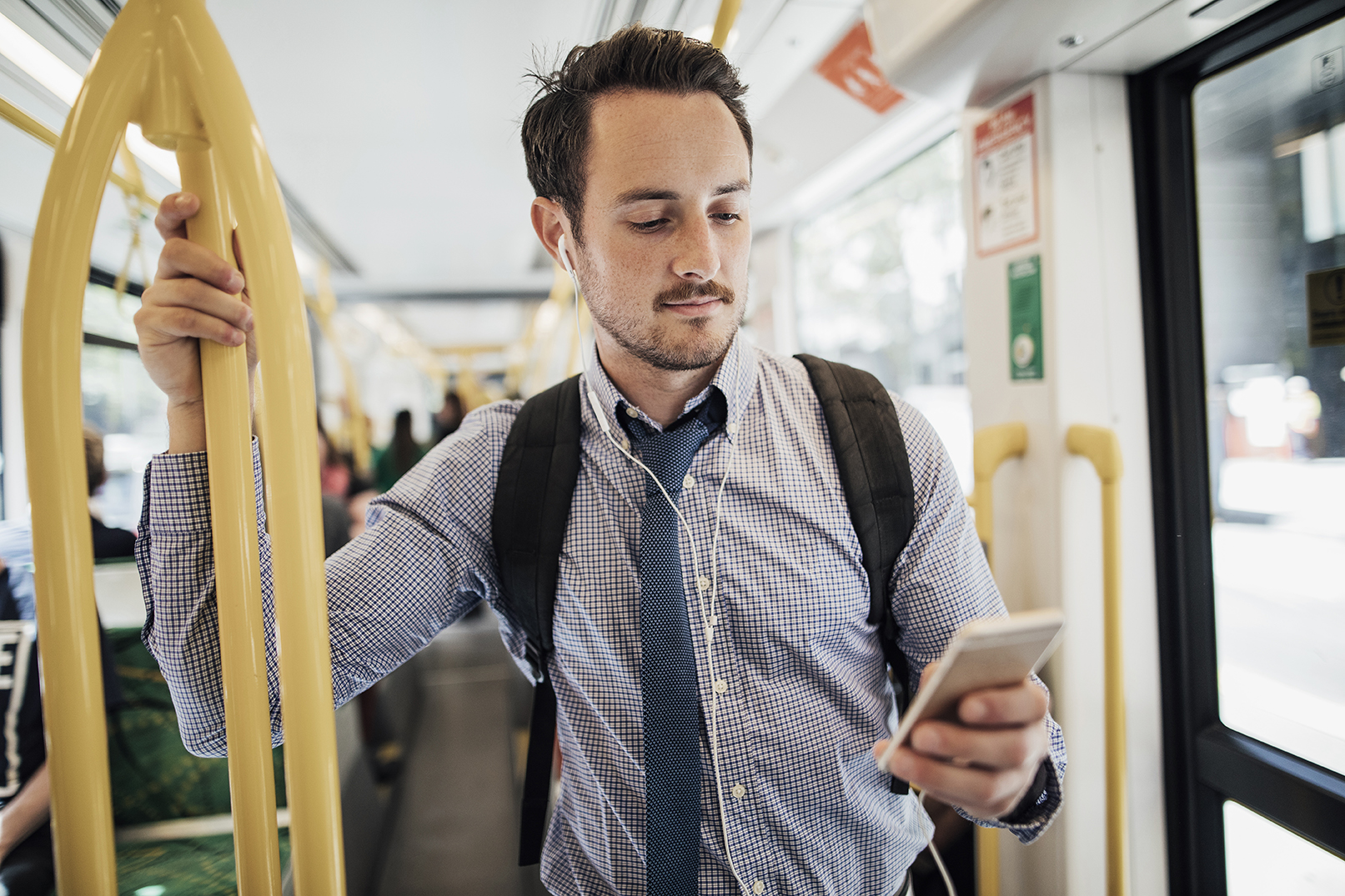 Mann steht mit Smartphone im Bus.