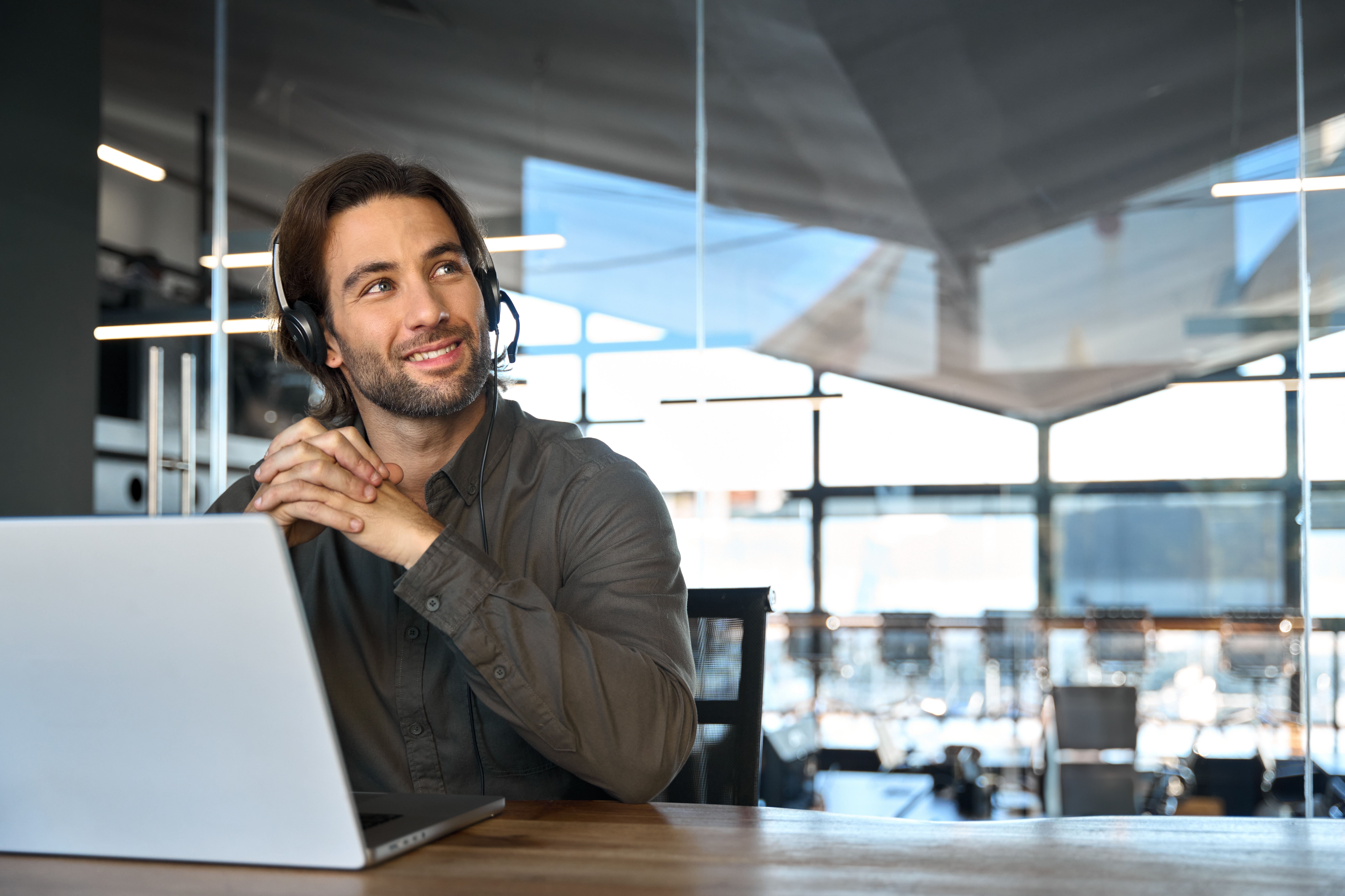 Mann sitzt vor einem Laptop und schaut nachdenklich lächelnd zur Seite.
