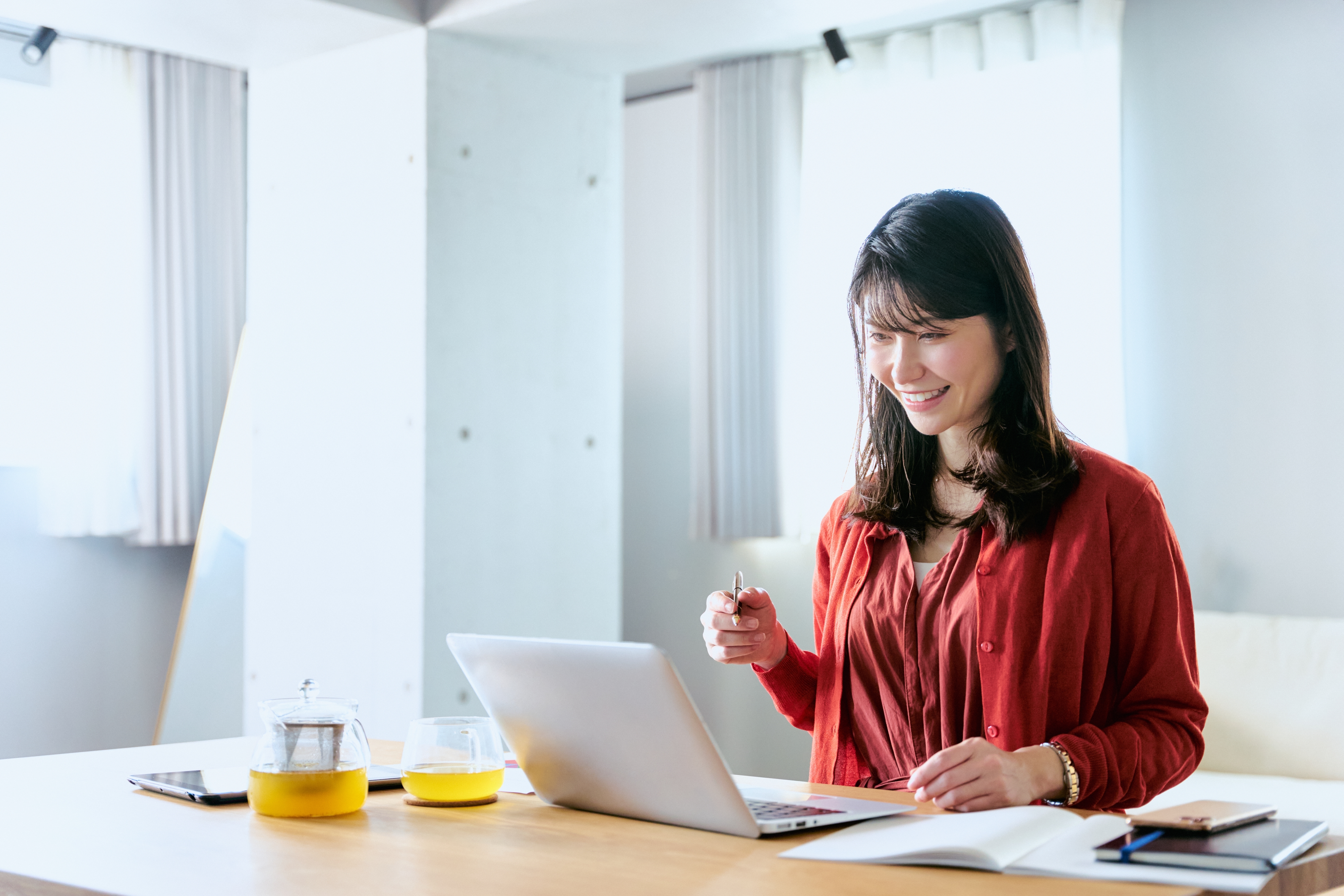 Frau sitzt und schaut lächelnd auf einen Laptop mit einem Stift in der Hand.