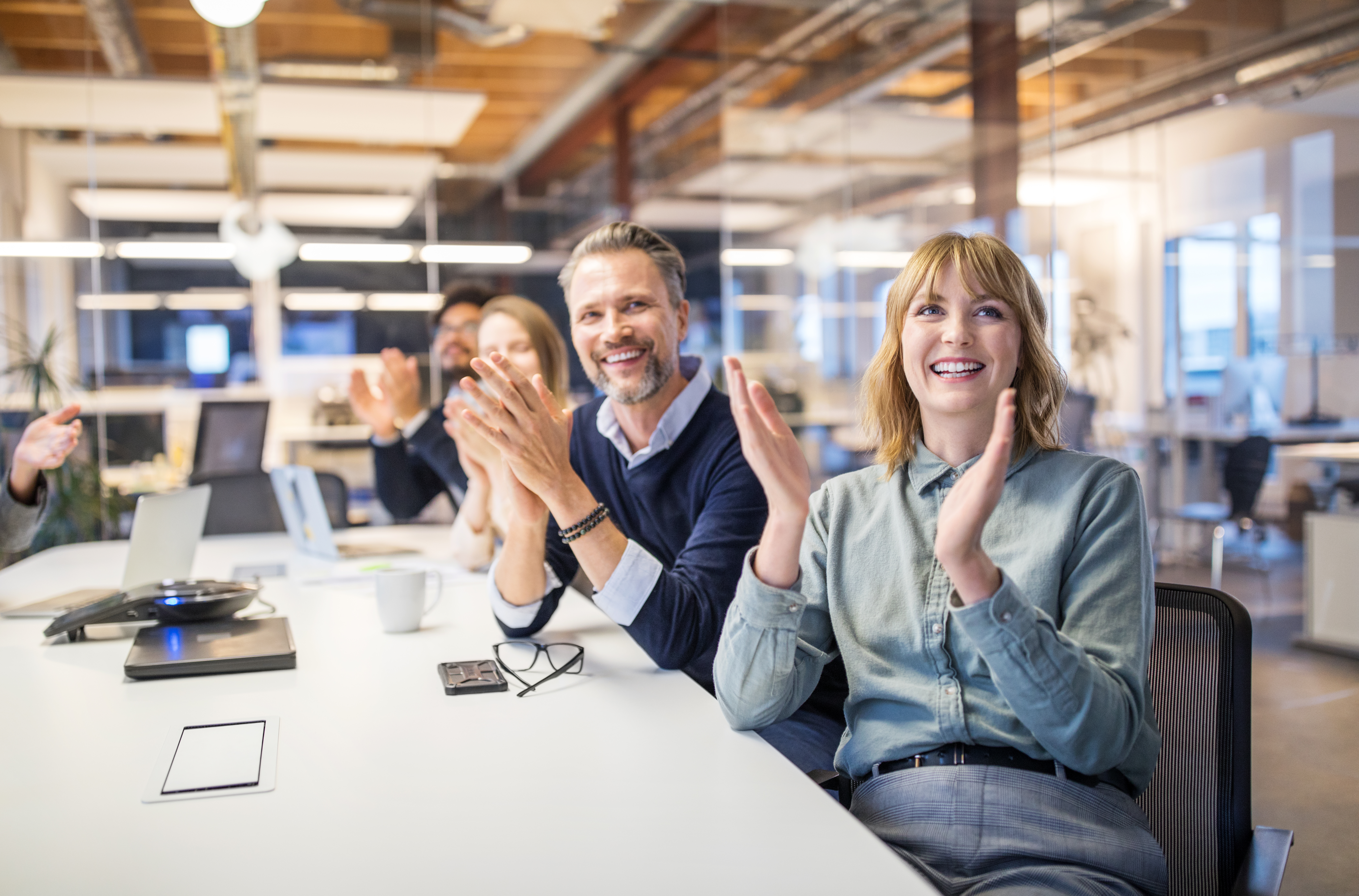 Mehrere Menschen sitzen im Büro zusammen und klatschen.