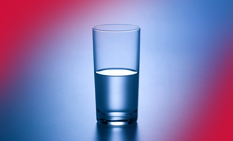 Glass of water half full or empty on gradient blue and red background