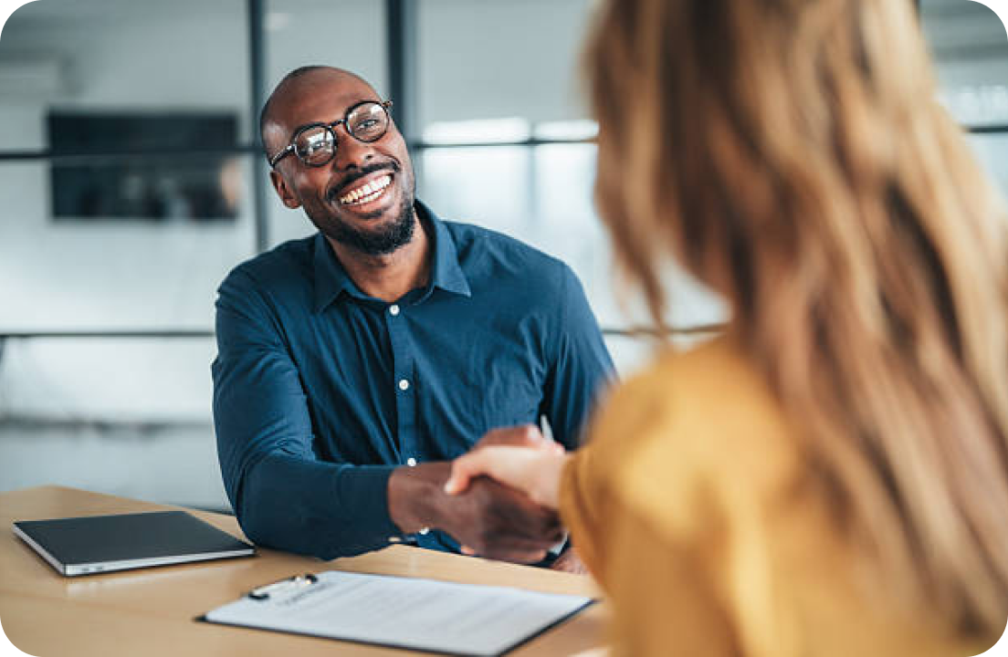 A loan officer smiling and shaking hands with a client across a desk