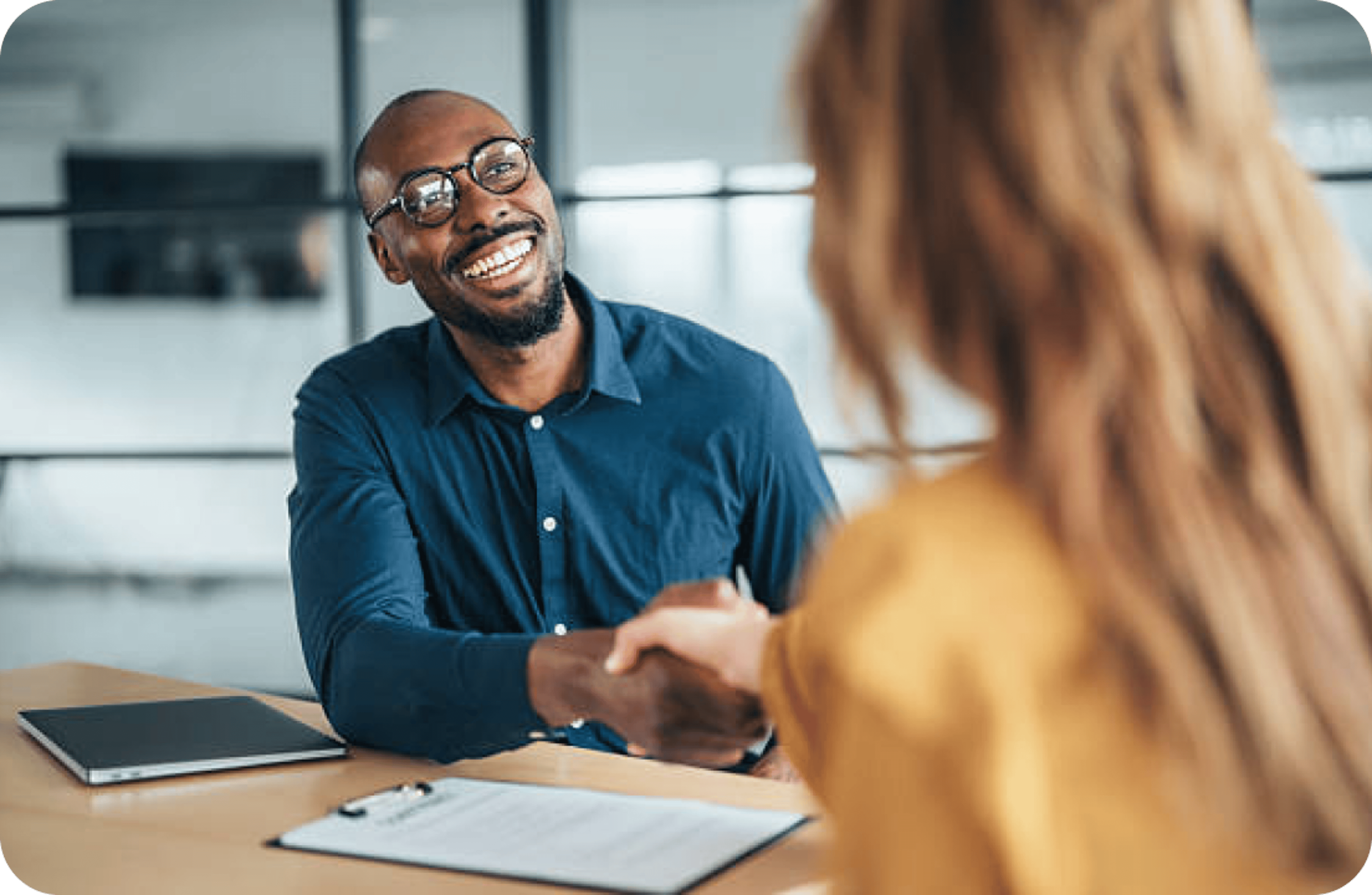 A loan officer smiling and shaking hands with a client across a desk