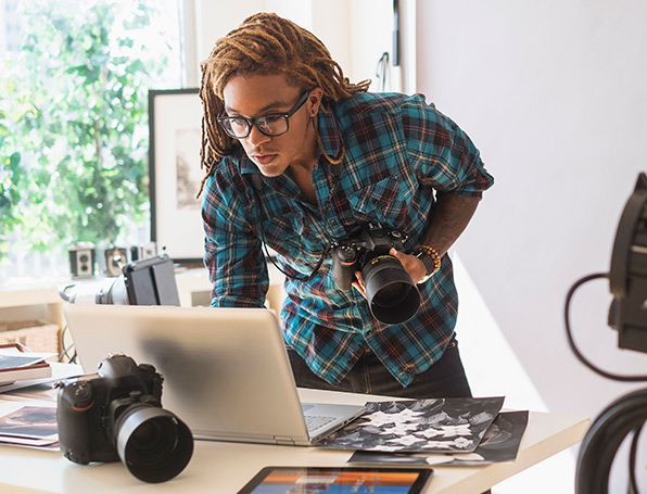 Sqre|Man holding a camera, looking at pictures on a laptop