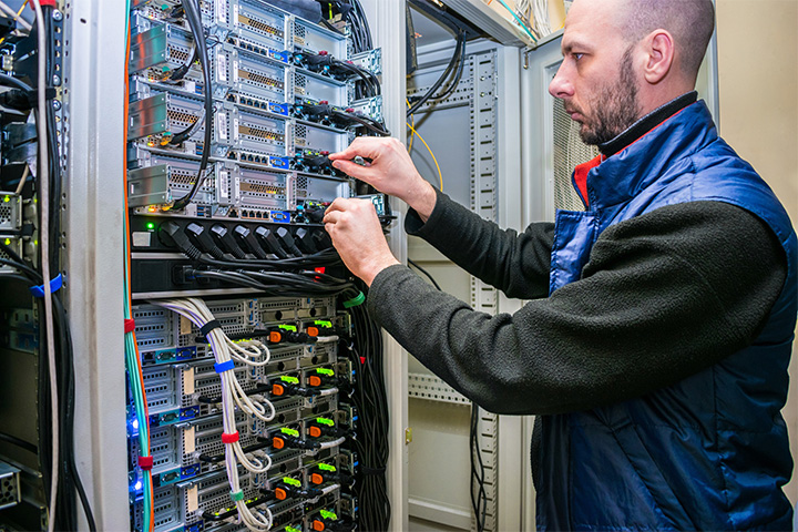 Tile|Network engineer switches power cables in the server room rack. The system administrator works in the data center. Portrait of a technician working with computer equipment.