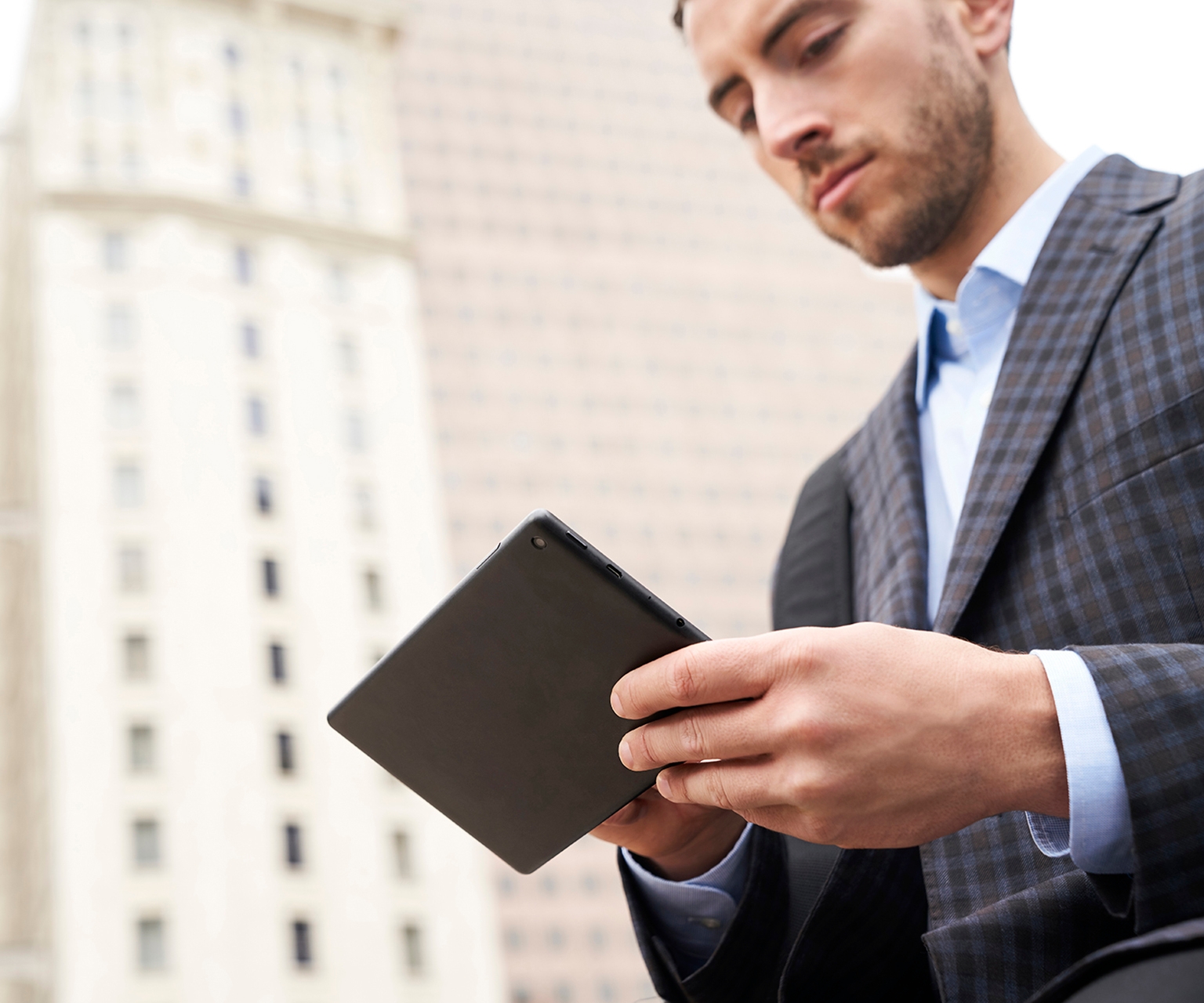 Tile | Man standing outside in a city looking at a tablet