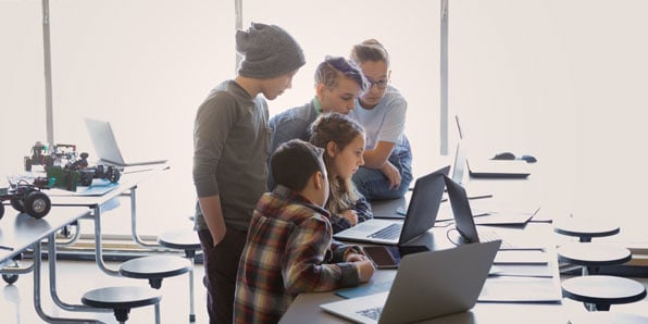Students looking at a laptop in a cafeteria.