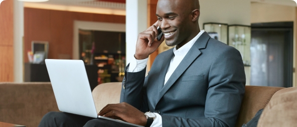 Full|Man sitting in a hotel lobby talking on the phone and using a laptop