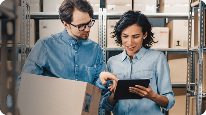 Wide| Man and woman standing in a warehouse, looking at a tablet