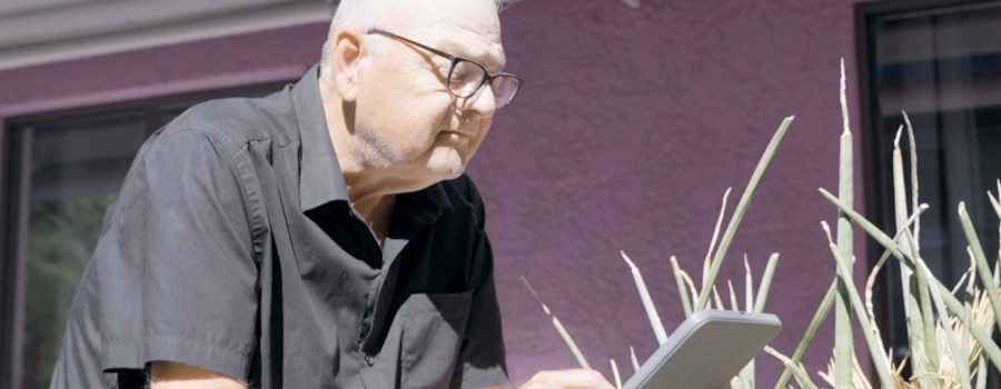 Wide|A man in glasses looking at a tablet outdoors.