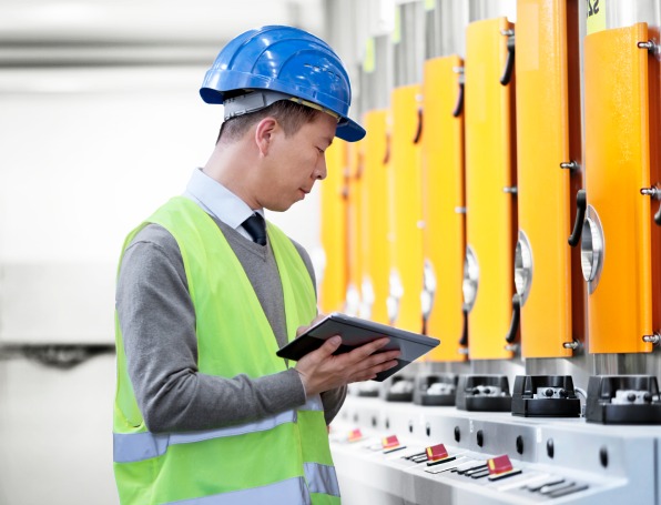 Card | A person in a hard hat holding a tablet and looking at machinery