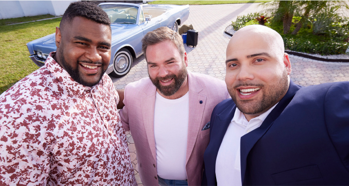 Three smiling men taking a selfie wearing stylish outfits while on vacation. 