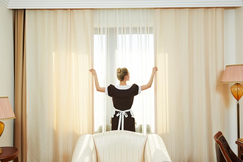 A young self employed house cleaner closing the blinds to keep the sunlight out.