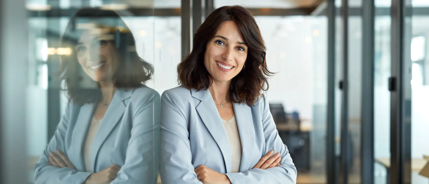 Mujer-ejecutiva-sonrie-a-la-camara-apoyada-en-un-ventanal-de-oficina.webp