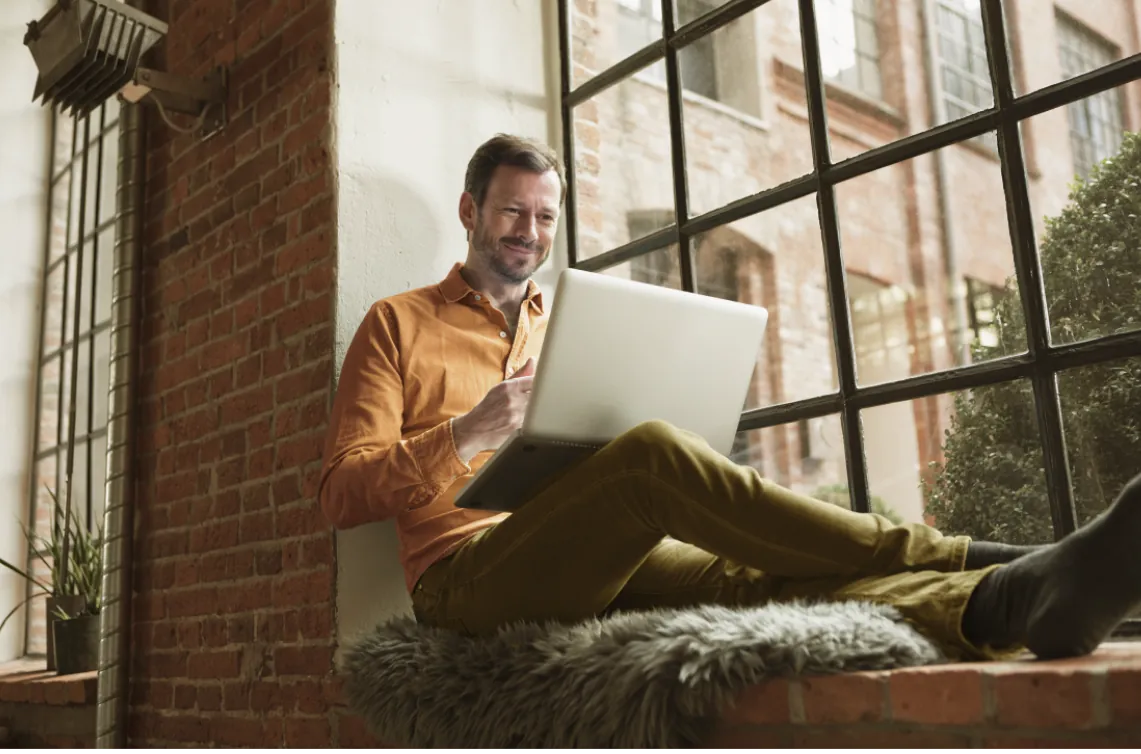 Hombre viendo computador sentado en una ventana