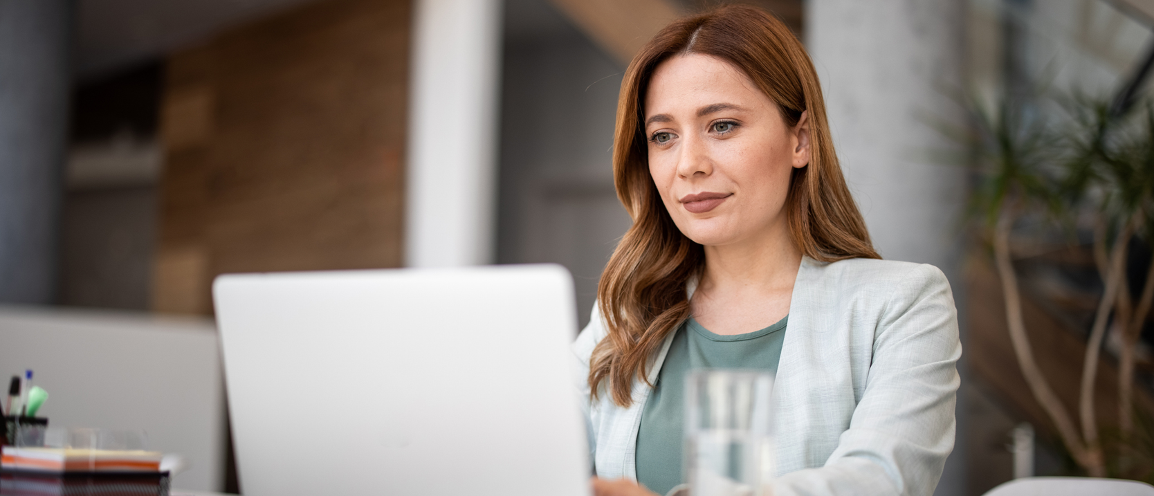 Mujer-ejecutiva-mira-contenta-la pantalla-de-su-computador-dentro-de-su-oficina.webp