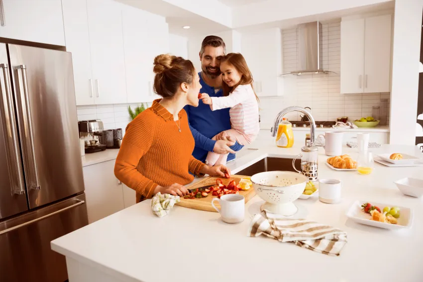 Un padre sostiene a su hija en brazos mientras ella le da un trozo de fruta a su madre