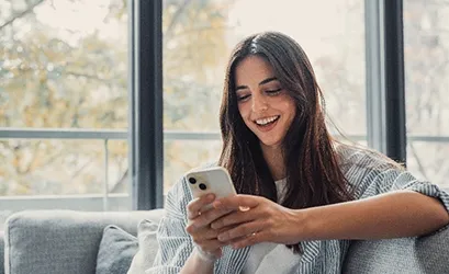 mujer sonriendo sentada en su sofá mirando el celular