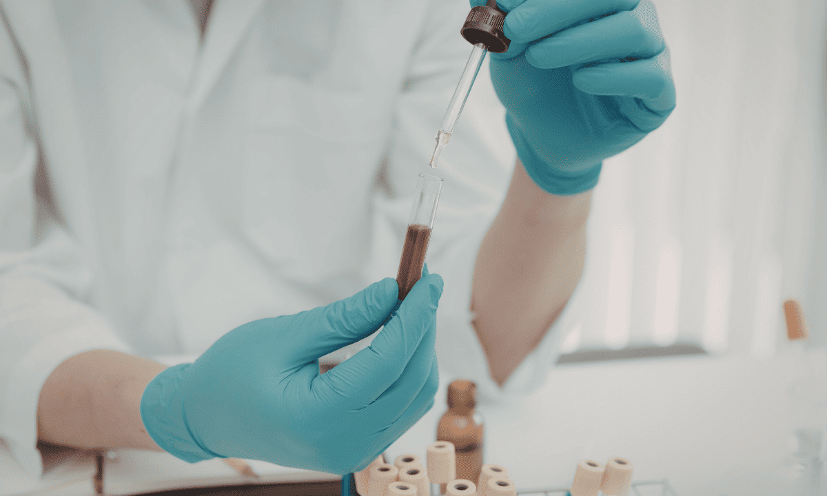 Close-up of a laboratory professional in blue gloves using a dropper to transfer a sample into a test tube, representing diagnostic methods such as blood testing.