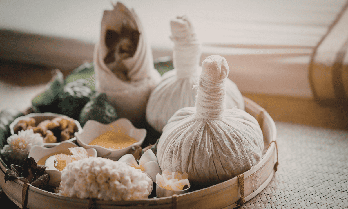 A wellness tray containing traditional herbal massage compresses, flowers, and natural powders used for holistic therapy.