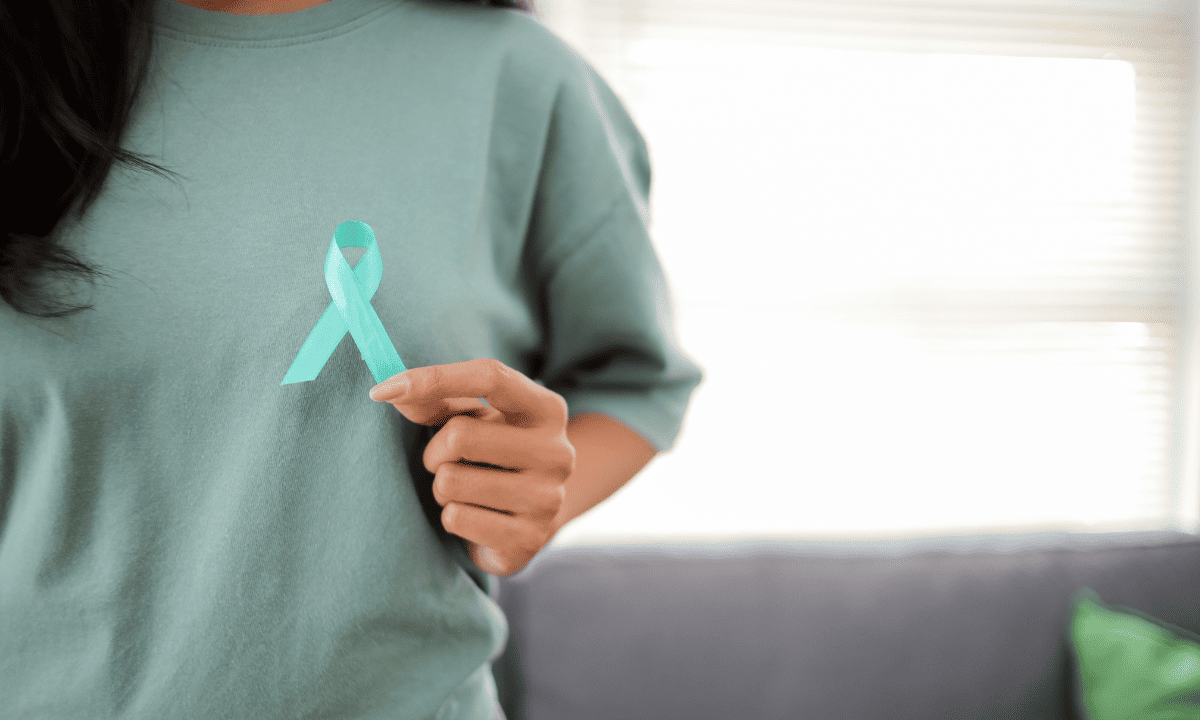Close-up of a woman in a green shirt holding a teal cervical cancer awareness ribbon.