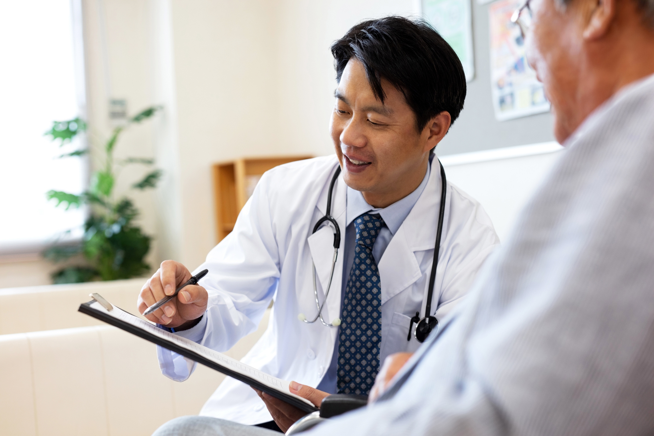 asian male doctor with stethoscope around neck showing a clipboard to an elderly patient doctor consultation health screening preventative care