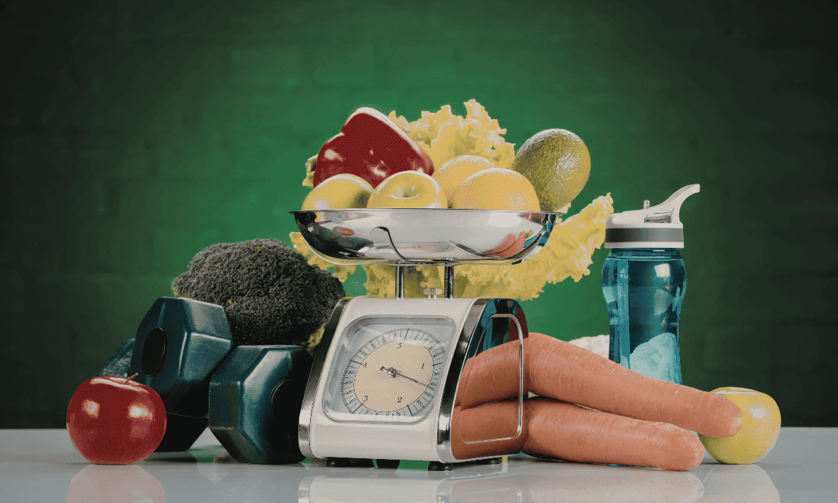 A lifestyle photo featuring a kitchen scale holding fresh fruit, flanked by vegetables like broccoli and carrots, a water bottle, and dumbbells, emphasizing the importance of diet and exercise.