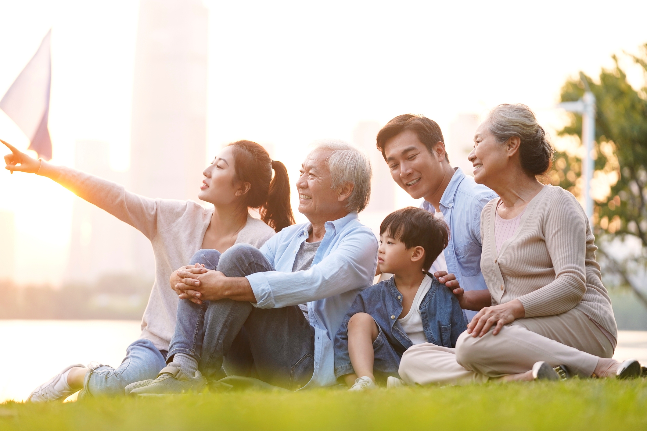 asian family three generations grandfather grandmother father mother son sitting on the grass at the park looking at the sunset