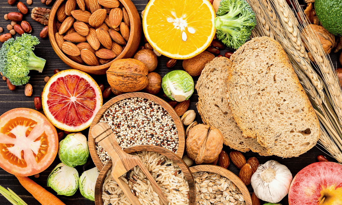 A top-down arrangement of various healthy foods, including whole grains, nuts, seeds, citrus fruits, and green vegetables.