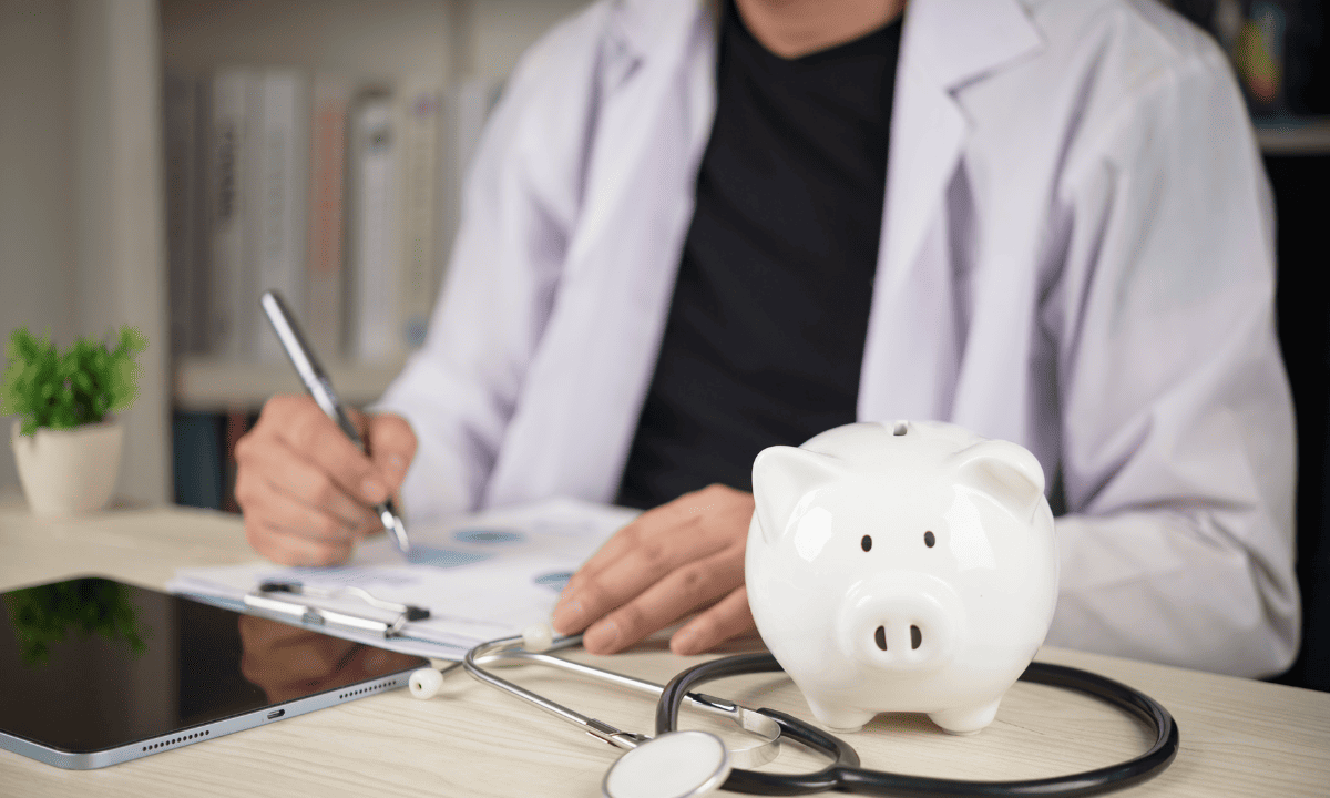 A doctor sitting at a desk with a stethoscope and a white piggy bank, symbolizing the financial considerations of nasal polyp removal.