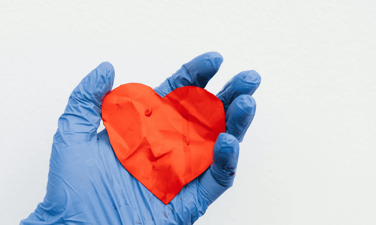 A hand in a blue medical glove holds a crumpled red paper heart, symbolizing the care and attention given to reproductive health and pain.