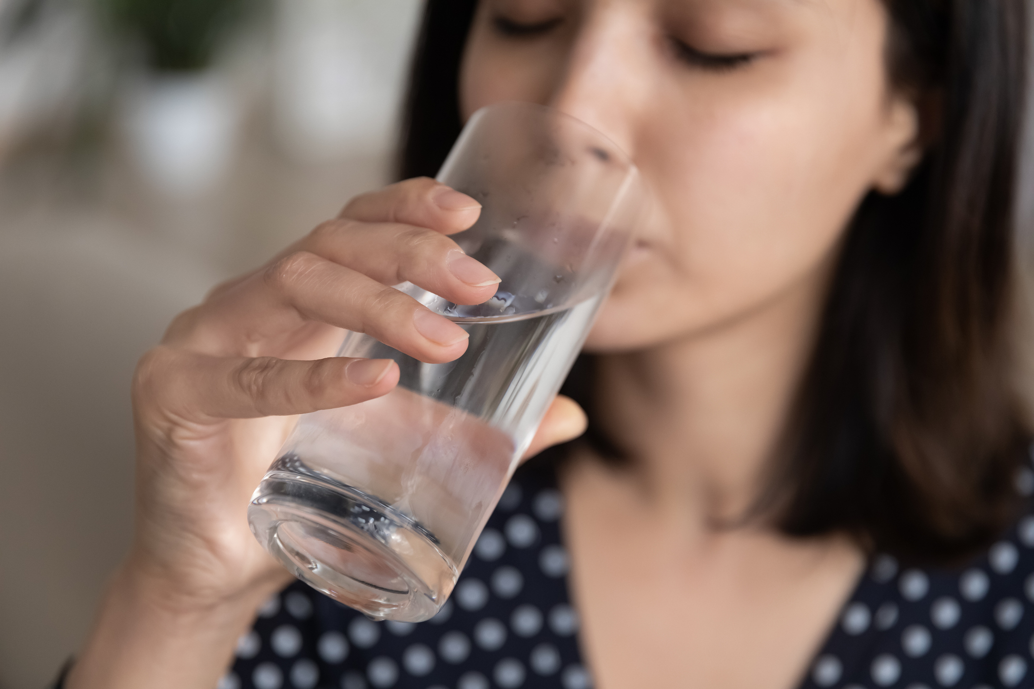 asian woman holding a glass cup half full with water and taking a drink hydration