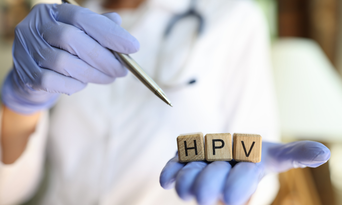A doctor holds wooden blocks spelling out HPV while pointing with a pen.