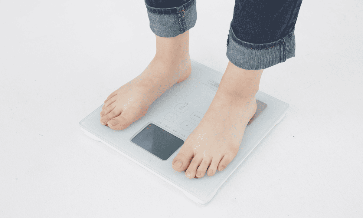 A person standing barefoot on a modern digital glass scale to measure their weight.