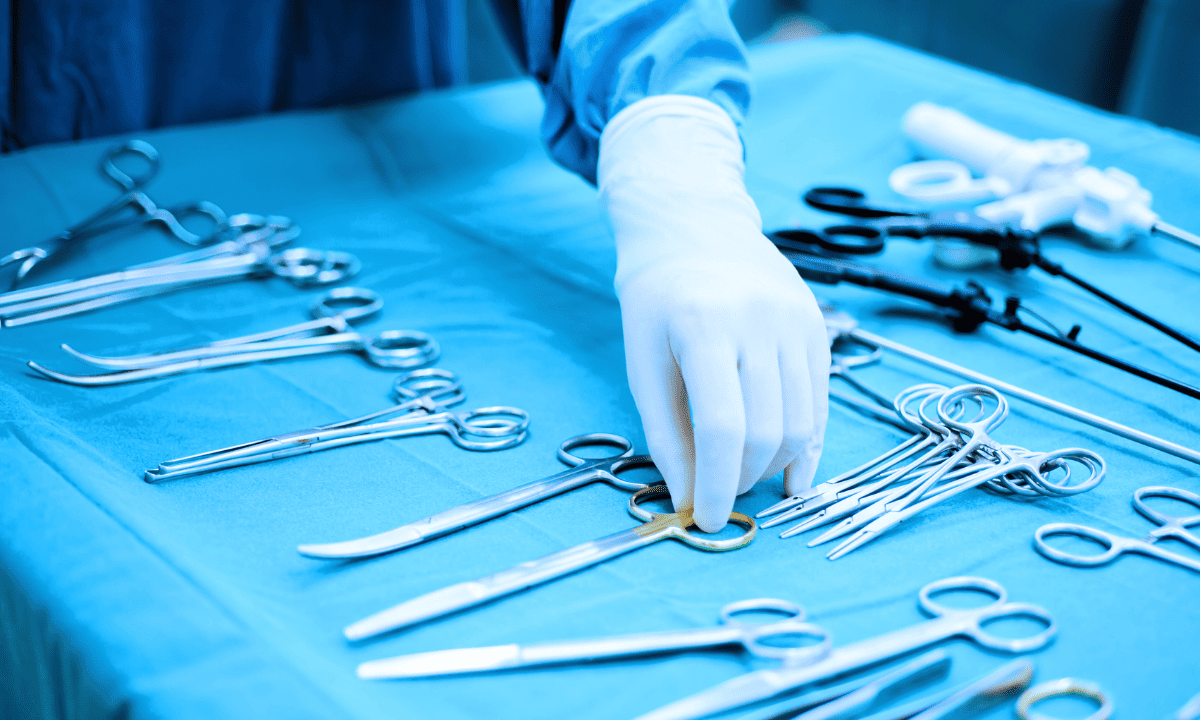 A gloved hand reaching for specialized stainless steel surgical instruments laid out on a blue sterile tray.