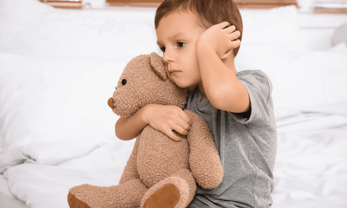 A child holding a teddy bear and covering his ear